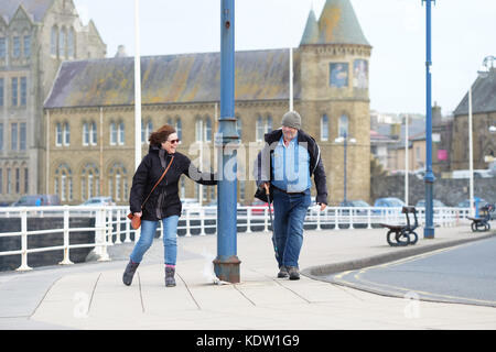 Aberystwyth, Ceredigion, Wales, UK. 16 Okt, 2017. UK Wetter. Ein paar es schwer zu gehen, da Sie auf der Promenade in die starken Winde biegen Sie an Aberystwyth auf der West Wales Küste als Sturm Ophelia Ansätze mit lokalen Winden von mehr als 50 km/h. Foto Steven Mai/Alamy leben Nachrichten Stockfoto