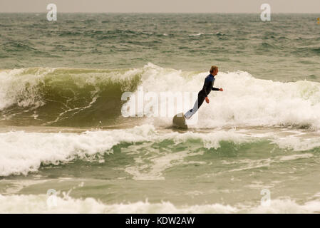 Surfer in einen Taucheranzug im Winter einer Welle und am Rande des Absturzes in das Meer in Boscombe, Bournemouth, Dorset, Großbritannien. Stockfoto