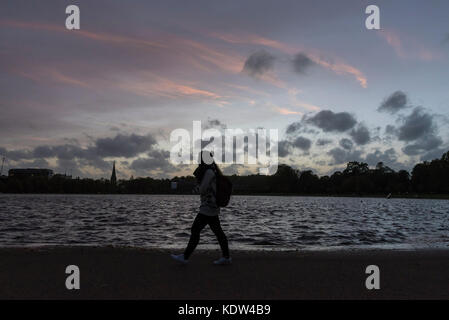 London, Großbritannien. 16. Oktober 2017. UK Wetter: Sonnenuntergang über dem runden Teich im Park Kensington Gardens. Staub durch Winde aus Hurrikan Ophelia brachte verursacht die Sonne eine geheimnisvolle Farbe orange gegen einen rötlichen Himmel erscheinen. Credit: Stephen Chung/Alamy leben Nachrichten Stockfoto