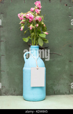 Malte blaue Flasche mit Kraft lable. grunge Grün Holz- Hintergrund. alte Flasche tag Mock-up. blaue Kanne mit rosa Rosen. Stockfoto