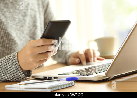 Nahaufnahme einer Frau Hände über ein Telefon und einen Laptop auf einem Tisch zu Hause Stockfoto