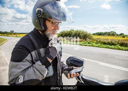 Mann Motorradfahrer in Schutzhelm auf Smartphone Display auf der Straße in der Nähe von seinem Fahrrad Stockfoto