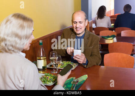Positive senior Paar beschäftigt mit Handys auf Datum im Cafe Stockfoto