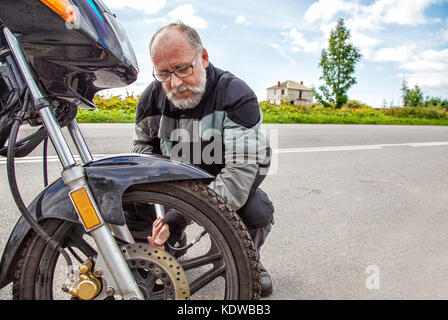 Älterer mann Rad draußen auf der Straße an einem sonnigen Tag von seinem Motorrad prüfen Stockfoto