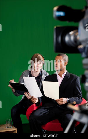 Floor Manager läuft durch Skripts mit einer Fernsehmoderatorin in einem Green Screen studio.tv Kamera unscharf im Vordergrund. Bewegungsunschärfe auf Stockfoto