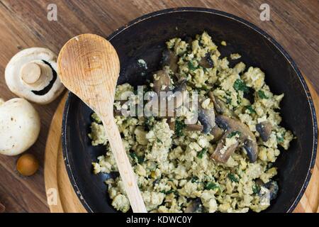 Eier mit Pilzen in Schwarz pan mit Holzlöffel Rührei Stockfoto