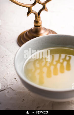 Fragment von Hanukkah und eine Schale mit Olivenöl auf einem weißen Tisch vertikal Stockfoto