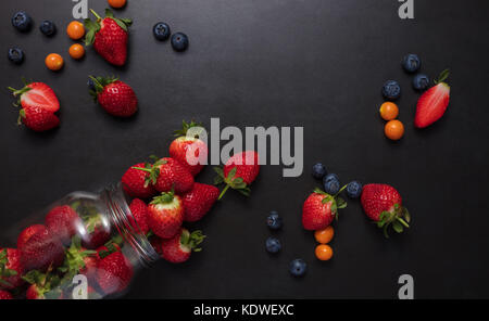 Frische Erdbeeren und Heidelbeeren auf schwarzem Hintergrund. Erdbeeren, aus einem Glas. Stockfoto