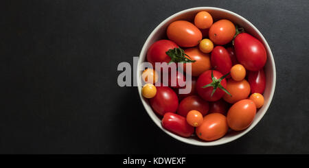 Schüssel mit Tomaten auf einem schwarzen Hintergrund. Meer Beeren mit Tomaten in eine Schüssel geben. Stockfoto