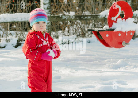 Attraktive Kleinkind oder kleine Mädchen im Schnee spielen, eine Schneeballschlacht und das Tragen eines hellen roten Schneeanzug. aktiven Lebensstil im Freien. Winter Urlaub. Stockfoto