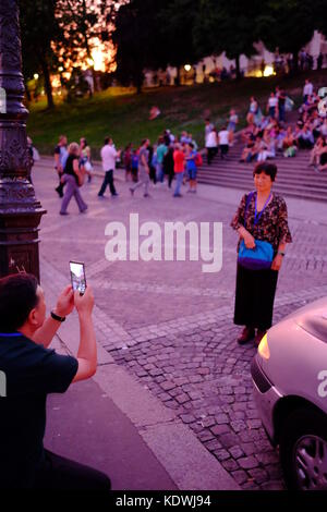 Ein Mann nimmt ein Foto von seiner Frau in Montmartre, Paris auf den Stufen von Sacre Coeur, mit seinem Smartphone Stockfoto