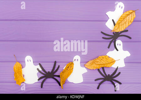 Die Gespenster, Spinnen und anderes Papier Silhouetten mit Blätter im Herbst Halloween Ecke Rahmen auf einem violetten Holztisch. Halloween Feier. Stockfoto