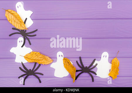 Die Gespenster, Spinnen und anderes Papier Silhouetten mit Blätter im Herbst Halloween Ecke Rahmen auf einem violetten Holztisch. Halloween Feier. Stockfoto