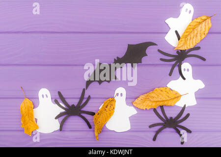 Die Fledermaus, Gespenster, Spinnen und anderes Papier Silhouetten mit Blätter im Herbst Halloween Ecke Rahmen auf einem violetten Holztisch. Halloween celebrat Stockfoto