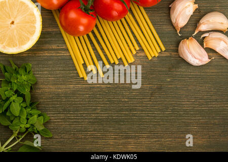 Raw italienische Küche Zutaten wie Nudeln spaghetti Knoblauch und Strauchtomaten mit Kopie Raum vor einem grünen Hintergrund Holz Stockfoto