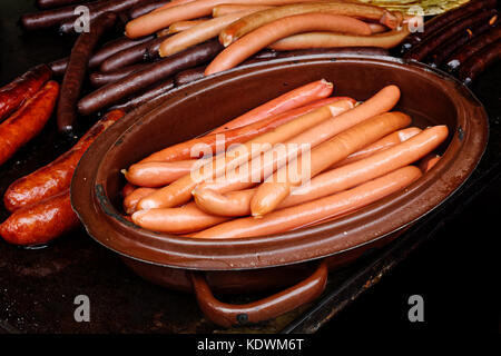 Gekochte Wiener Würstchen in Metall Topf Neben gegrillten Würstchen auf Gusseisen Bratpfanne. Stockfoto