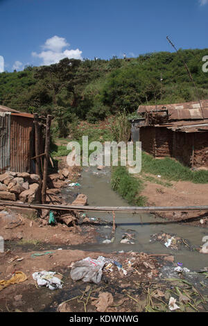 Ein verschmutzter Fluss mit Kanalisation und Plastikmüll, der durch zwei Baracken in den Kibera-Slums, Nairobi, Ostafrika, fließt Stockfoto