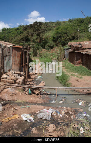 Müll um verschmutzten Fluss, der durch zwei Baracken in den Kibera Slums, Nairobi, Kenia, Ostafrika fließt Stockfoto