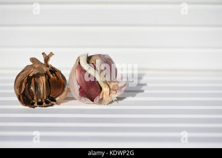 Essen Fotografie Bild von Schwarzen und Weißen öffnen Knoblauch Zwiebel und Knoblauchzehen in der Sonne mit weißem Holz Hintergrund und an der Südküste England Großbritannien Stockfoto