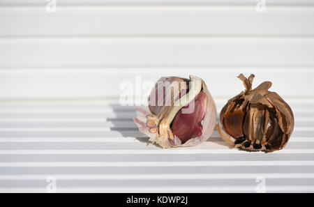 Essen Fotografie Bild von Schwarzen und Weißen öffnen Knoblauch Zwiebel und Knoblauchzehen in der Sonne mit weißem Holz Hintergrund und an der Südküste England Großbritannien Stockfoto