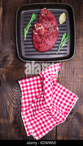 Rohes Rindfleisch Steak mit Gewürzen auf eine Schwarze Pfanne Grill mit einem Griff, braun Holz- Hintergrund Stockfoto