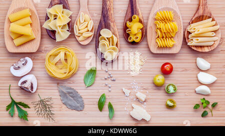 Italienisches Essen Konzept. verschiedene Nudelsorten in Holzlöffel mit Zutaten Basilikum, Tomate, Knoblauch, Petersilie, Lorbeer, Pfeffer, Champignon und Stockfoto