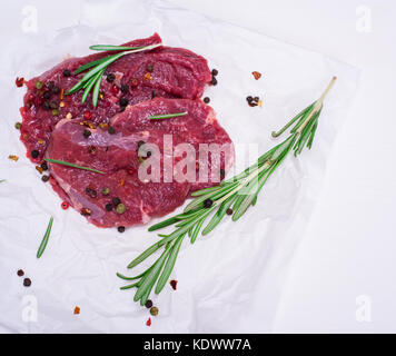 Rohes Rindfleisch Steaks mit Gewürzen und Rosmarin auf weißem Papier, leeren Raum auf der rechten Seite Stockfoto