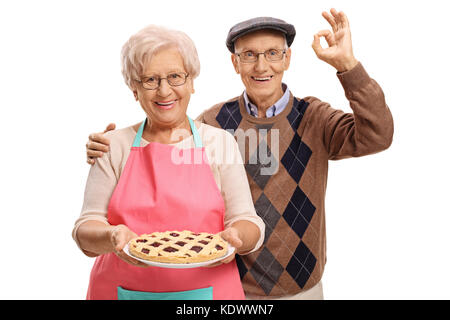Ältere Frau mit einem frisch gebackenen Kuchen und ein älterer Mann, der ein OK-Zeichen auf weißem Hintergrund Stockfoto