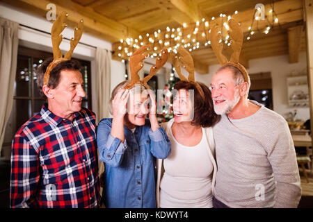 Ältere Freunde tragen zu Weihnachten Stirnbänder mit Rentiergeweih und haben Spaß. Stockfoto