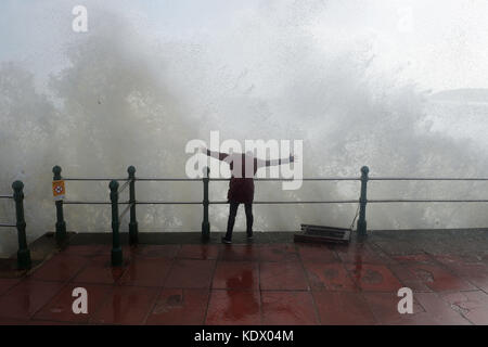 Eine Frau sprankt, als Wellen an der Meereswand in Penzanze, Cornwall, aufprallen, als Hurrikan Ophelia Großbritannien und Irland mit Böen von bis zu 80 mph trifft. Stockfoto