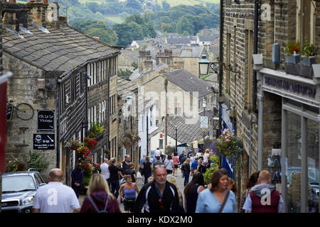 Pennines Dorf, Haworth in West Yorkshire, England. Touristen mischen sich auf der Main Street einen steilen gepflasterten Straße mit interessanten Geschäften Stockfoto