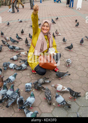 Eine malaysische Muslimin füttert Tauben im Courtyard, bevor die Batu Höhlen komplexe in Gombak, Selangor, Malaysia. Stockfoto