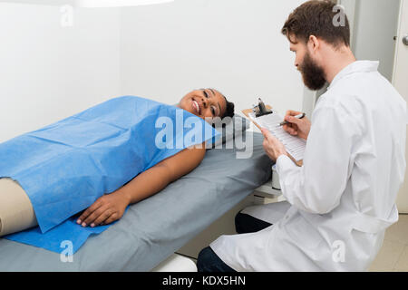 Portrait von weiblichen Patienten liegend auf Bett, während Arzt holding Zwischenablage im Krankenhaus Stockfoto