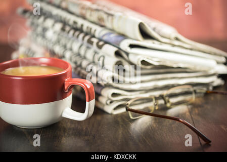 Stapel Zeitung auf Holz- Hintergrund mit Tasse Kaffee und Gläser Stockfoto