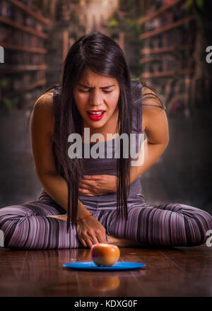 Schöne und einsame Mädchen leiden unter appetitanregend, Schmerzen in seinem Magen wenn sie sieht eine Apple über einen blauen Platte, in einer verschwommenen Hintergrund Stockfoto