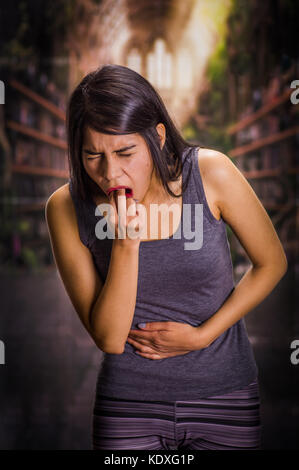 Schöne und einsame Mädchen leiden der appetitanregend, ihren Magen zu halten und seine Finger in den Mund zu bewegen, zu Erbrechen, ein Hintergrund verschwommen Stockfoto