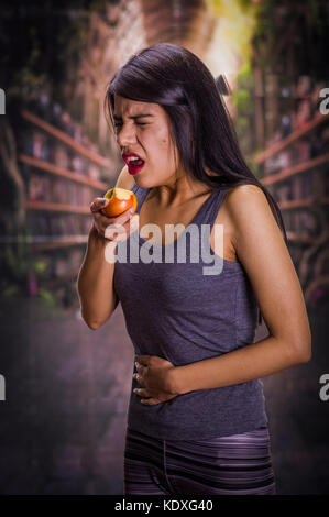 Schöne und einsame Mädchen leiden unter appetitanregend, Schmerzen in seinem Magen während Sie das Essen eines Apfels, in einem verschwommenen Hintergrund Stockfoto