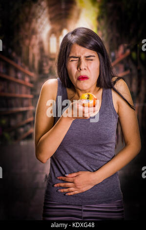 Schöne und einsame Mädchen leiden unter appetitanregend, Schmerzen in seinem Magen wenn Sie sich einen Apfel und Tun ekelhaft Gesichter, in einem verschwommenen Hintergrund Stockfoto