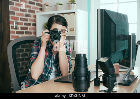 Junge hübsche Studentin Holding professionelle Kamera Praxis Unternehmen Bild in Fotograf Unternehmen sitzen arbeiten Büro Schreibtisch. Stockfoto