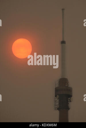 Emley Moor Mast mit Sand in der Luft über die uk durchgebrannt durch Sturm Ophelia, die eine helle rote Sonne über Großbritannien, kirklees, West Yorkshire erscheinen, Stockfoto