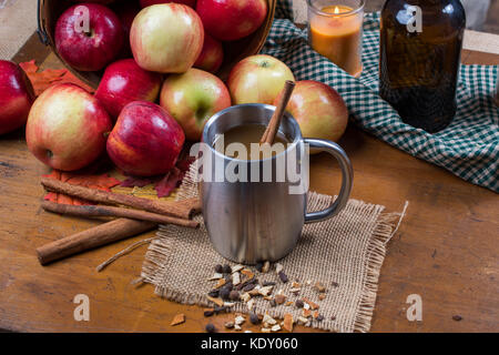 Silver Cup mit Apple Cider. Äpfel und Zimtstangen im Hintergrund sind. Schale sitzt auf der Leinwand mit Gewürzen für rustikale Einstellung Stockfoto