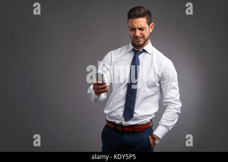 Ein hübscher junger Mann verärgert Gefühl beim halten und mit Blick auf sein smartphone Stockfoto