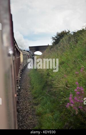 Blick entlang der Außenseite der Dampfzug aus dem Fenster, da es eine Brücke über die Eisenbahn poppy North Norfolk Line angefahren Stockfoto