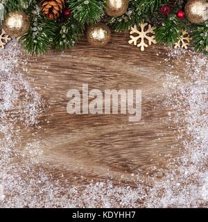 Weihnachten oberer Rand mit goldenen Ornamenten, Niederlassungen und Schnee Rahmen auf eine rustikale Holz Hintergrund Stockfoto