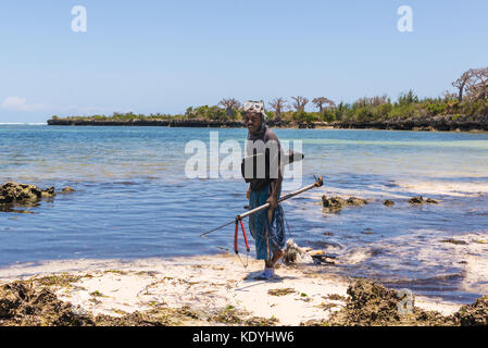 Afrikanische Speer fischer Rückkehr von einem Tag von Angeln Wandern auf einer unberührten tropischen Strand mit Baobab im Hintergrund. Pemba, Sansibar, Tansania Stockfoto