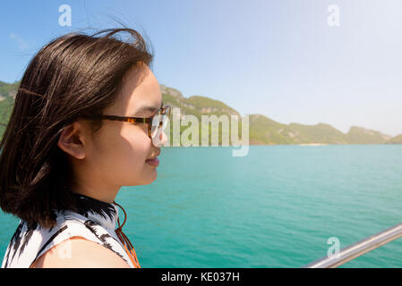 Nette junge Frau mit Brille glücklich lächelnd auf dem Boot während der Fahrt die Natur der Insel und unter Sonneneinstrahlung im Sommer an Mu Ko Ang Thong Stockfoto