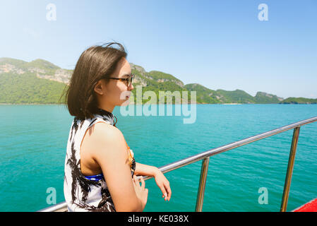 Nette junge Frau mit Brille glücklich lächelnd auf dem Boot während der Fahrt die Natur der Insel und unter Sonneneinstrahlung im Sommer an Mu Ko Ang Thong Stockfoto