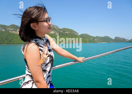 Nette junge Frau mit Brille glücklich lächelnd auf dem Boot, während die schöne Natur der blauen Himmel und Meer Kreuzfahrt im Sommer an Mu Ko Ang Thong Stockfoto