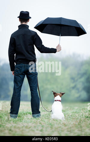 Freundschaft zwischen Hund und Besitzer im Regen stehen mit Schirm Stockfoto