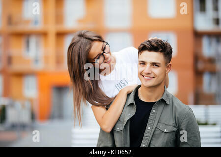 Schöne junge Paar in Sonnenbrille an einander suchen und lächelnd beim Stehen im Freien. Mädchen huckepack Stockfoto